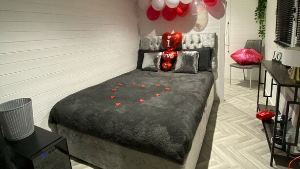 Un dormitorio con cama, mesita de noche, lámpara, silla y estante en la pared.