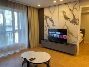 A modern hotel room with a large TV on a wall, a small round table, and a bed with a headboard.