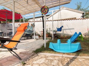 Eine Terrasse mit Schaukel, Hängesessel und einem roten Sonnenschirm.