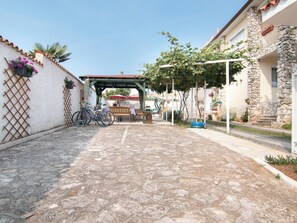 A cobblestone pathway leading to a covered seating area with a bench and tables, surrounded by buildings with stone facades and potted plants. - Apartment 354 by Interhome (Fažana)