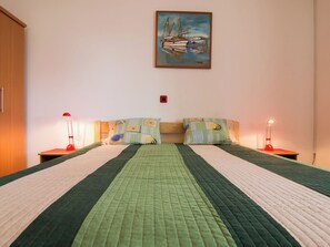 Ein Doppelbett mit einer grünen Tagesdecke, zwei Nachttische mit roten Lampen und ein Bild von Booten an der Wand.