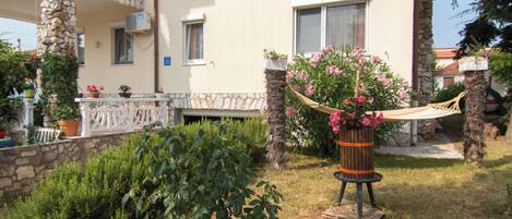 A building with a stone facade, a balcony with a white railing, and a hammock in the garden.