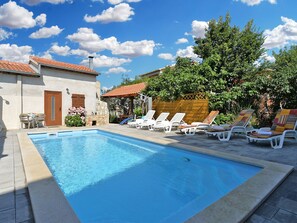 Ein Swimmingpool mit Liegestühlen und ein Gebäude mit Steinbauweise und einem Ziegeldach.