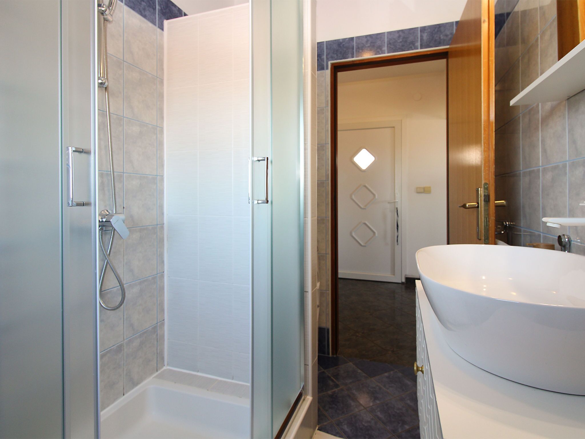 Un baño con cabina de ducha de vidrio, un lavabo blanco y una puerta que da a otra habitación.