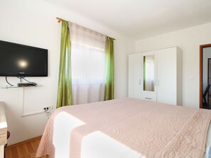 Ein Hotelzimmer mit Bett, Wandfernseher, Kleiderschrank und einem Fenster mit Vorhängen.