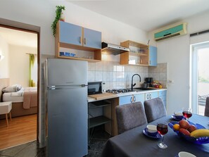 Eine moderne Küche mit Kühlschrank, Mikrowelle, Herd und Spüle. Ein Essbereich mit Tisch für zwei Personen und eine kleine Sitzecke mit einer Couch.