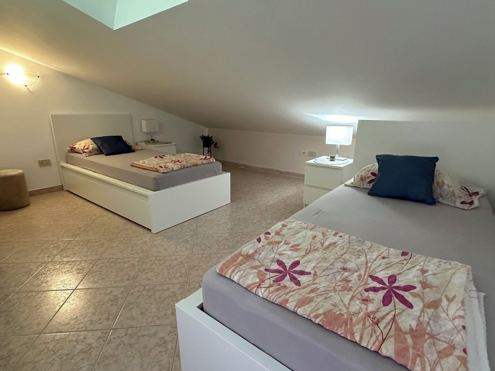 Un dormitorio con una cama, una cama individual, una mesita de noche, una lámpara, una planta en maceta y una luz en el techo.