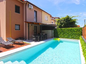 Piscina com espreguiçadeiras, mesa e área de varanda coberta.