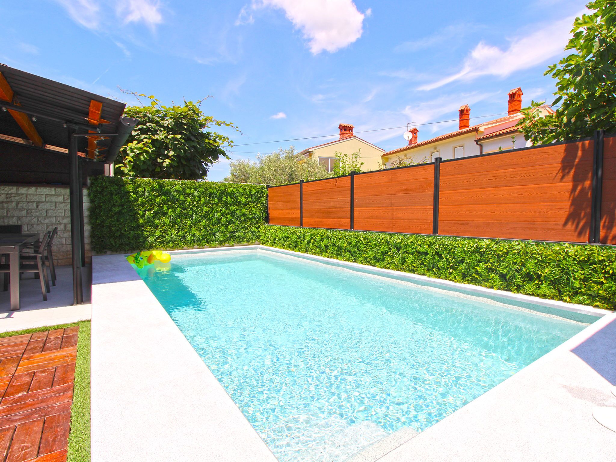 A rectangular swimming pool with a wooden deck and a brick wall.