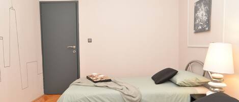 A bedroom with two beds, a door, a bedside table with a lamp, and a wall-mounted picture.