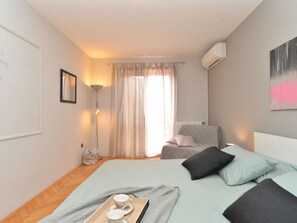 A bedroom with a bed, a chair, a bedside table, a lamp, a window with curtains, and an air conditioning unit. - House 843 by Interhome (Fažana)