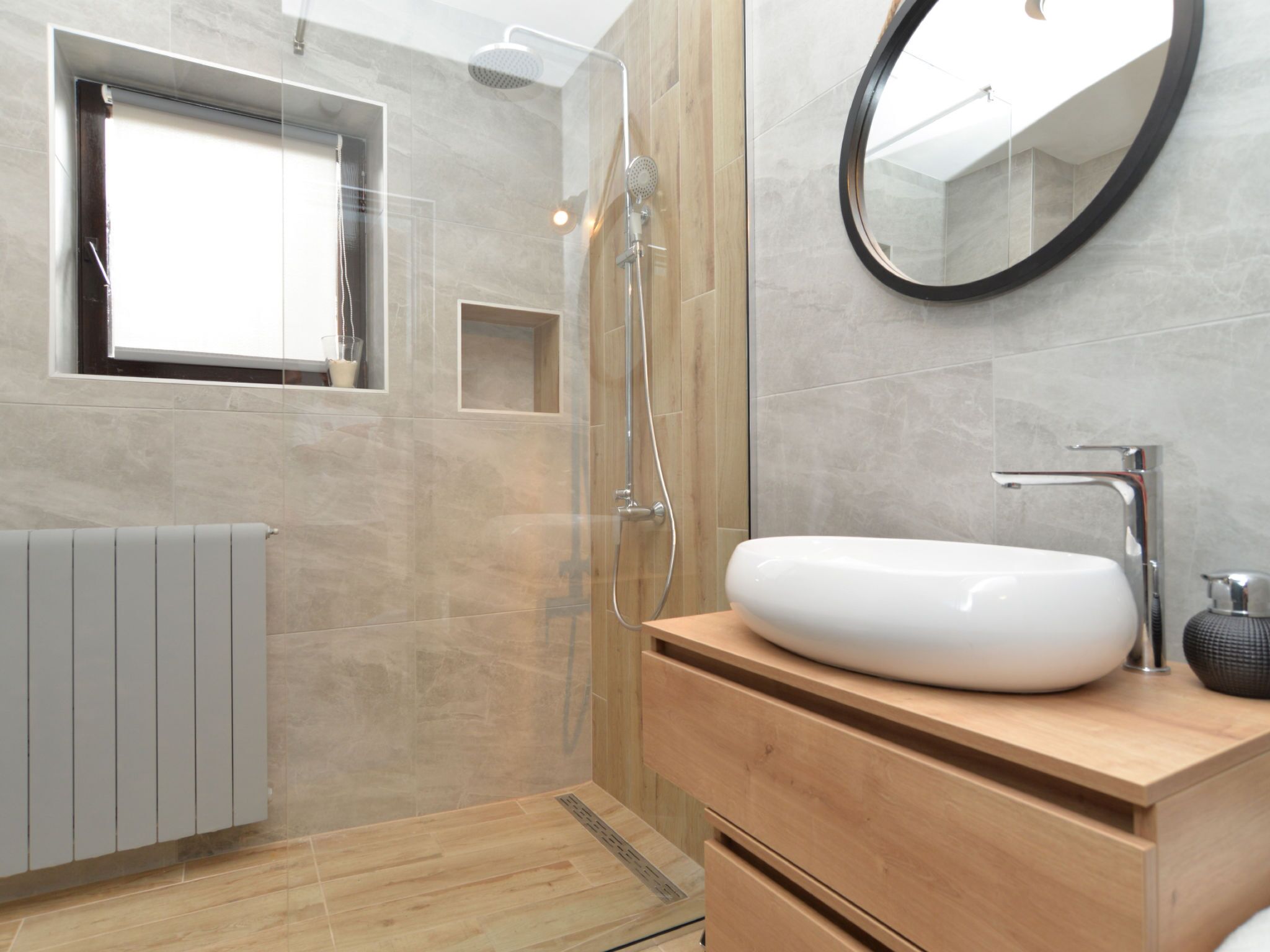 A modern bathroom with a shower, a sink, a mirror, and a window.