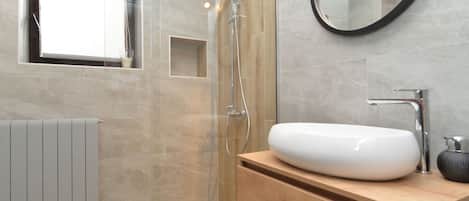 A modern bathroom with a shower, a sink, a mirror, and a window.