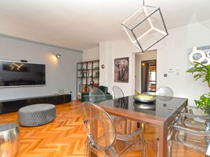 A modern living room with a flat-screen TV, a dining table with chairs, a glass coffee table, and a decorative elephant painting. - House 843 by Interhome (Fažana)
