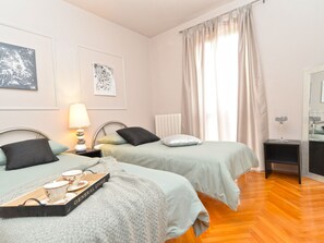 A hotel room with two beds, a bedside table with a lamp, a small side table, a mirror, and artwork on the walls. - House 843 by Interhome (Fažana)