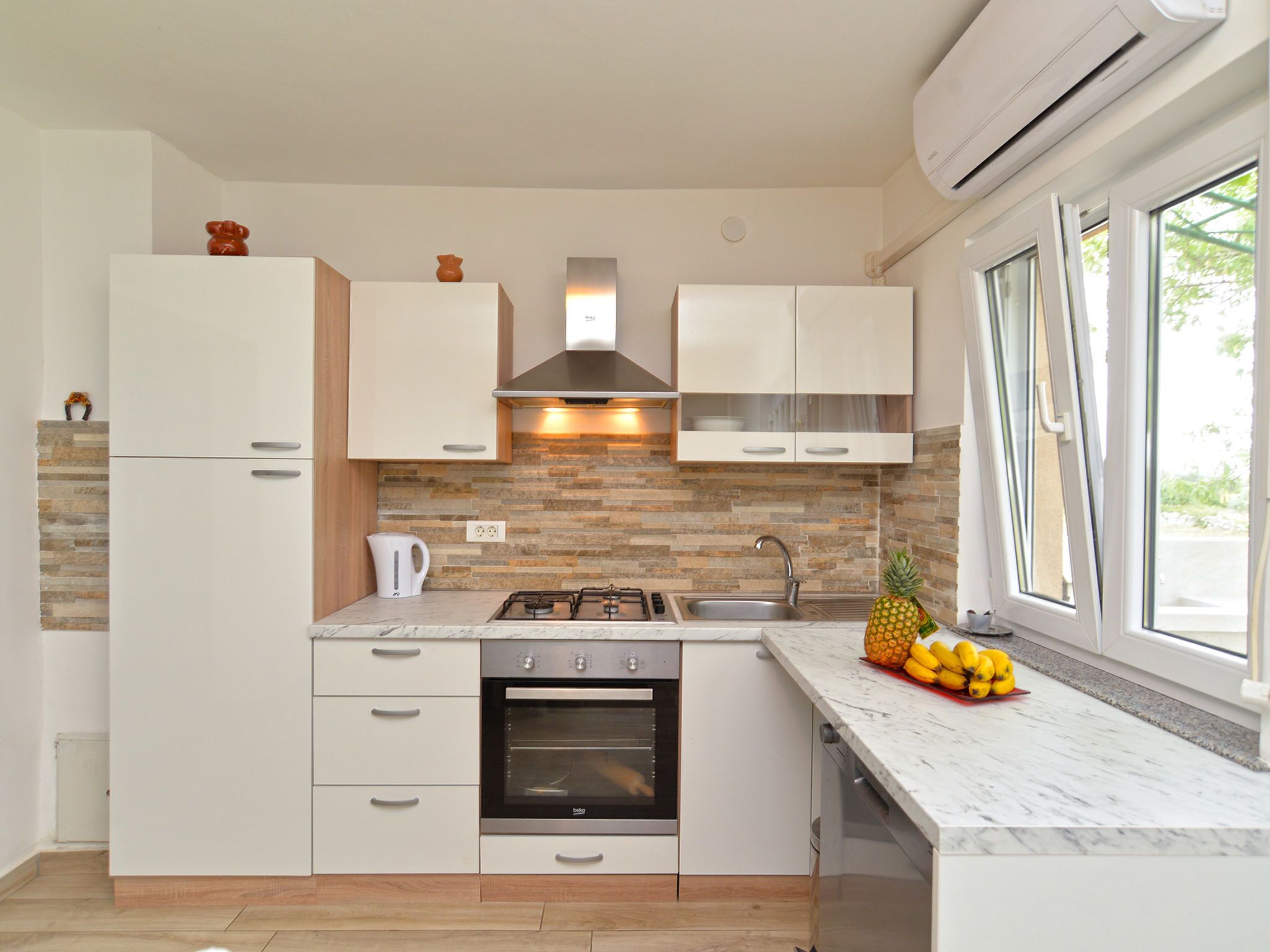 Une cuisine moderne avec des meubles blancs, une cuisinière à gaz, un four, un évier et une fenêtre donnant sur un beau paysage.