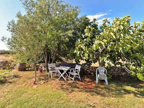 An outdoor seating area with a table and chairs, surrounded by trees and a stone wall. - House 1691 by Interhome (Fažana)