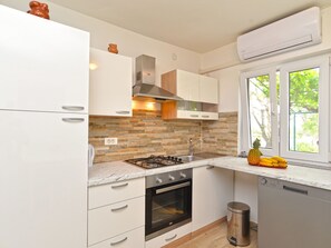 Eine moderne Küche mit weißen Schränken, einem Gasherd, einem Backofen, einem Geschirrspüler und einem Fenster mit Blick auf Grünflächen.
