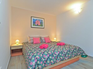 Ein Schlafzimmer mit geblümtem Bettbezug, zwei Nachttischlampen, einem gerahmten Bild an der Wand und Holzboden.