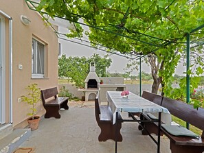 Eine Terrasse im Freien mit Tisch, Bänken, Grill und einem Blumentopf.