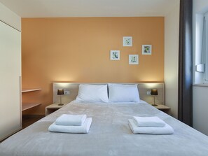 Une chambre d’hôtel avec un grand lit, deux tables de chevet avec des lampes, une armoire et des œuvres d’art accrochées au mur.
