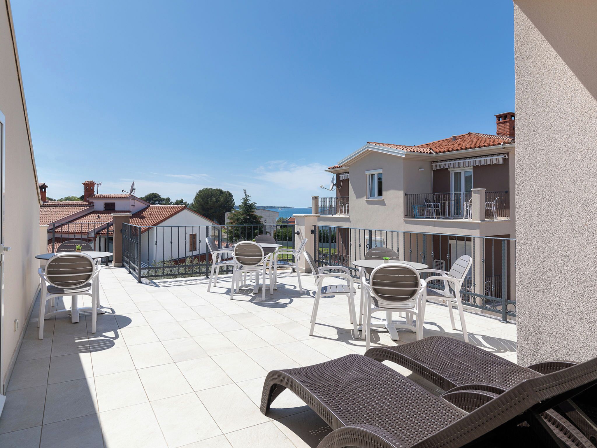 Una terraza con mobiliario exterior, vista al mar y un edificio con balcón.