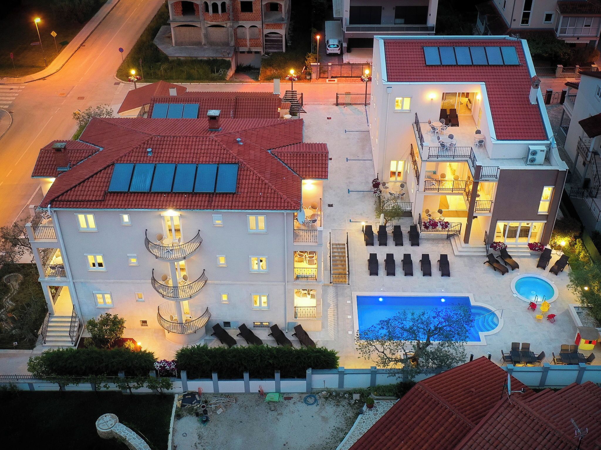 A multi-story hotel with a swimming pool, outdoor seating, and a well-lit entrance.