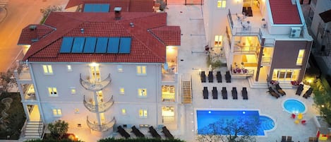 A multi-story hotel with a swimming pool, outdoor seating, and a well-lit entrance.