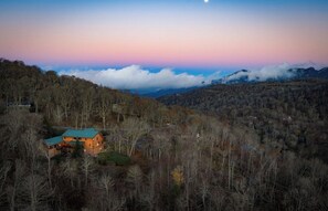 A lodge with a green roof nestled among trees, surrounded by a mountainous landscape. - 8 Bed 5 Bath Luxury Lodge-Free Resort Shuttle, HotTub, Sauna, Game Room, Theater (Sugar Mountain)