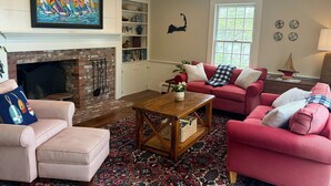 A living room with a fireplace, a red sofa, a striped armchair, and a colorful painting. - Waterfront Orleans Oasis with a Private Deep Water Dock (Orleans)