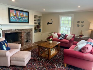Ein Wohnzimmer mit Kamin, einem roten Sofa, einem gestreiften Sessel und einem farbenfrohen Gemälde.