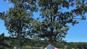 A deck with a wicker sofa, a wooden table, and an American flag. - Waterfront Orleans Oasis with a Private Deep Water Dock (Orleans)