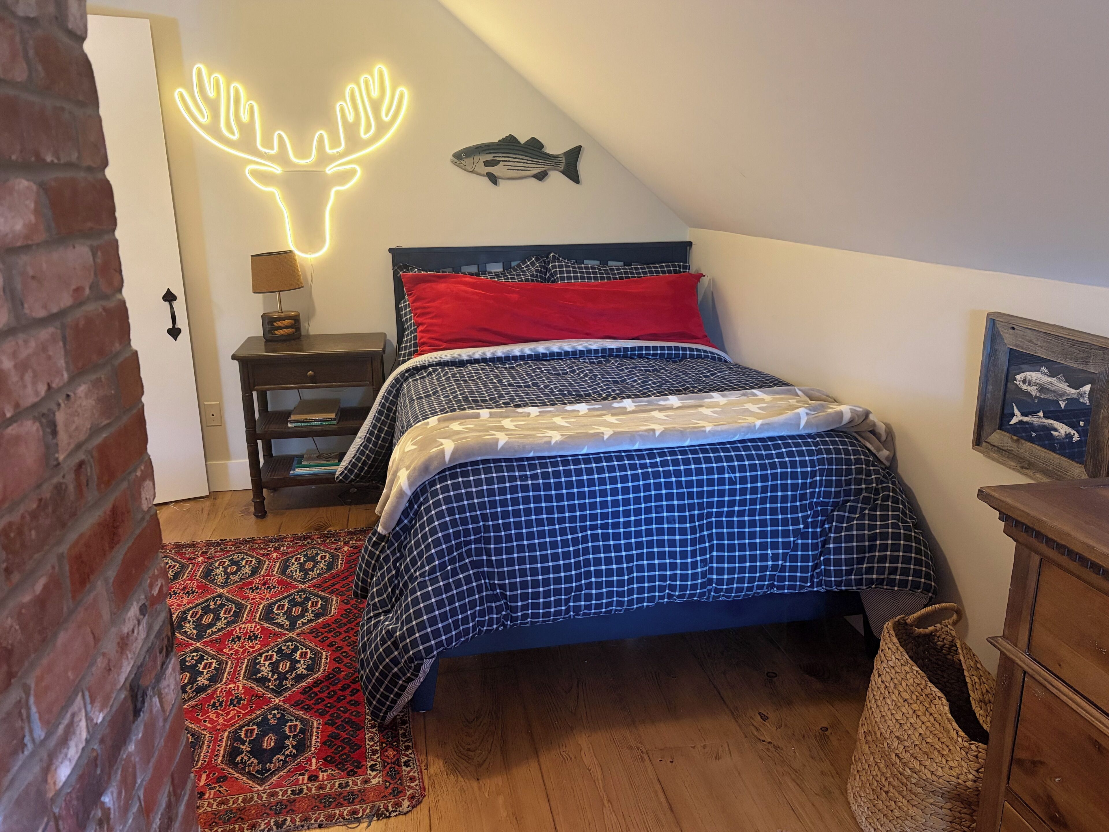 Ein Schlafzimmer mit einem Bett, einer Neon-Hirsch-Lampe, einer Fischdekoration, einem Teppich und Holzboden.