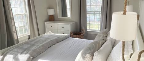 A bedroom with a bed, a dresser, a mirror, a lamp, and a window with curtains.