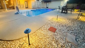 Un patio trasero con piscina, mobiliario de jardín y una casa.