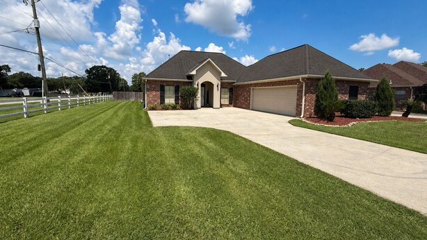 A residential house with a front yard, a garage, and a clear sky. - Welcome to Magnolia Pearls, a peaceful retreat for comfort and relaxation. (Prairieville)