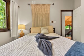A bedroom with a bed, a window with curtains, a lamp, a door, and a view of greenery outside. - Poconos Chalet: Hot Tub, Theater, EV & Lake Access (Pocono Lake)