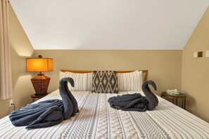 Hotelkamer met een bed, kussens, een lamp, een klein tafeltje en handdoeken gevouwen in de vorm van zwanen.