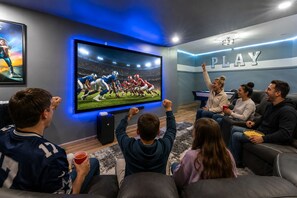 Een groep mensen kijkt naar een voetbalwedstrijd op een grote televisie in een kamer met een bord waarop 'PLAY' staat.
