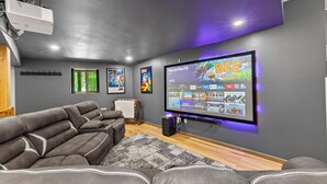 Una sala de cine en casa moderna con un televisor de pantalla plana grande, un sillón de cuero reclinable y un proyector montado en el techo.