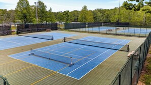 Un campo polisportivo con campi da tennis e badminton, circondato da una recinzione verde.