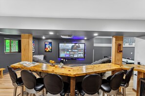 Ein Konferenzraum mit einem großen Flachbildfernseher, der eine Spieloberfläche zeigt, umgeben von schwarzen Stühlen und einem Holztisch.