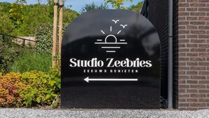 Ein schwarzes Schild mit weißer Schrift, das 'Studio Zeebries' und einen Pfeil anzeigt.