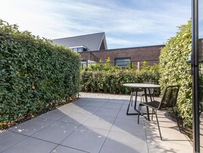 A patio area with a table and chairs, surrounded by a hedge and a building with a sloped roof. - Studio RustUit by Interhome (Koudekerke)