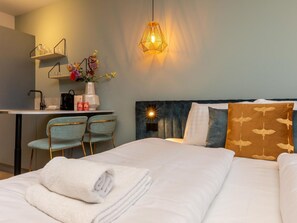 A hotel room with a bed, a desk with chairs, a hanging light fixture, and a wall-mounted shelf with items. - Studio RustUit by Interhome (Koudekerke)