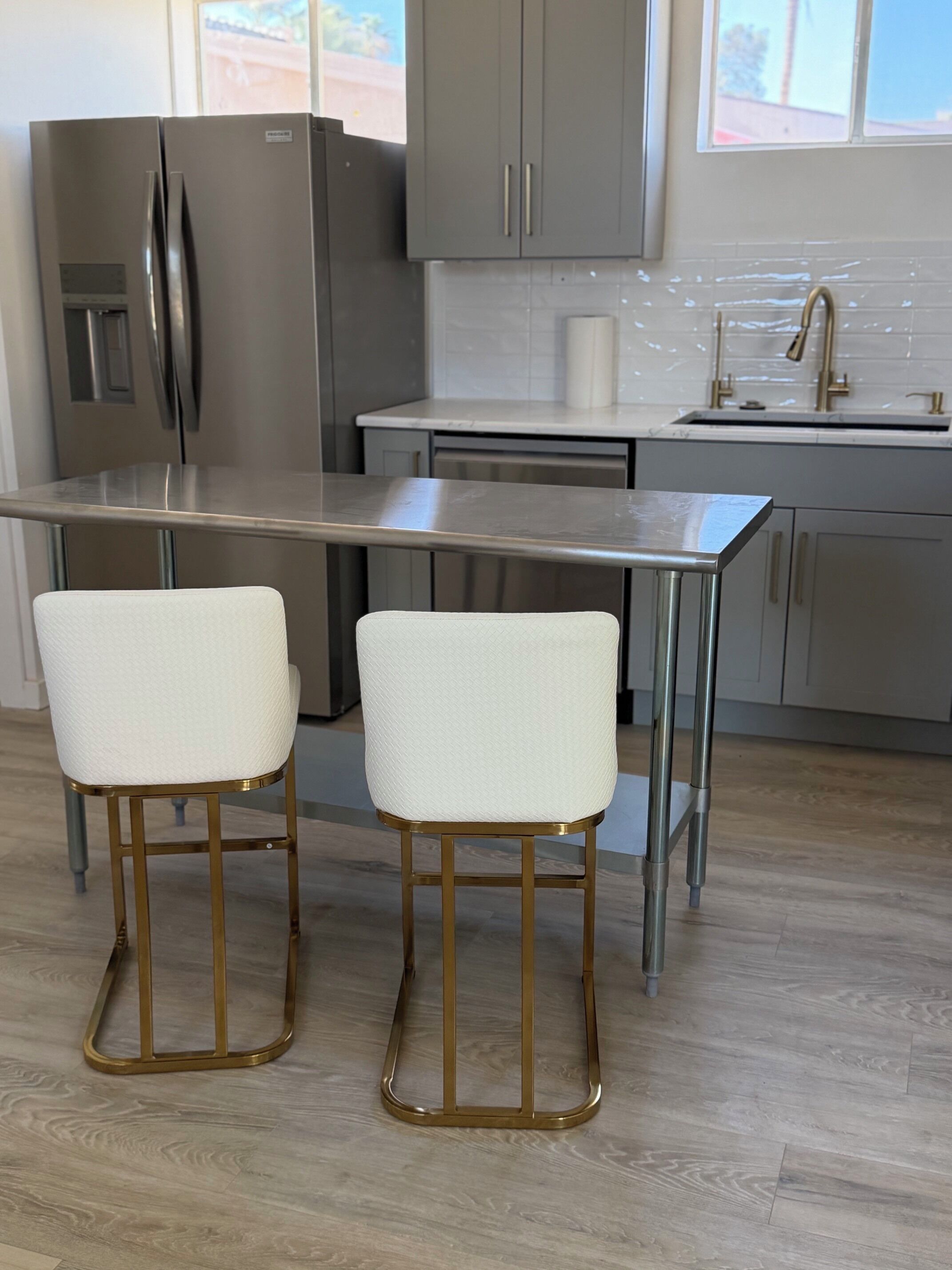 A modern kitchen with stainless steel appliances, a marble countertop, and two bar stools with gold legs.
