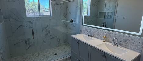 A modern bathroom with a glass-enclosed shower, a large vanity with a double sink, and a large mirror above the vanity.