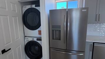Cocina compacta con refrigerador de acero inoxidable, lavadora y secadora integradas, y ventana que proporciona luz natural.