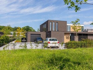 A modern building with a garage, a number 16 garage door, and a parking area with two cars. - Studio ZeeRust by Interhome (Koudekerke)