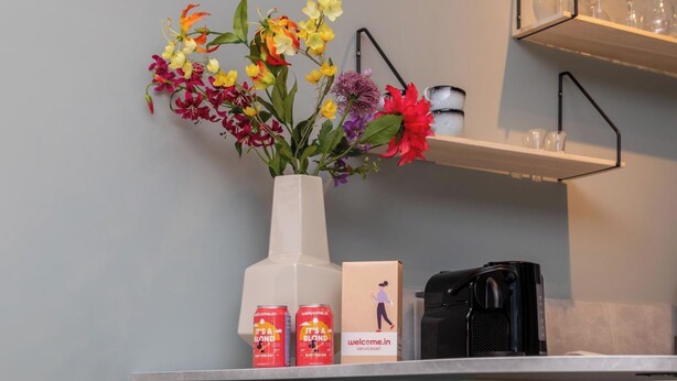 A room with a white vase of flowers, a coffee machine, and two cans of 'Welcome.in' beverage on a counter. - Studio ZeeRust by Interhome (Koudekerke)